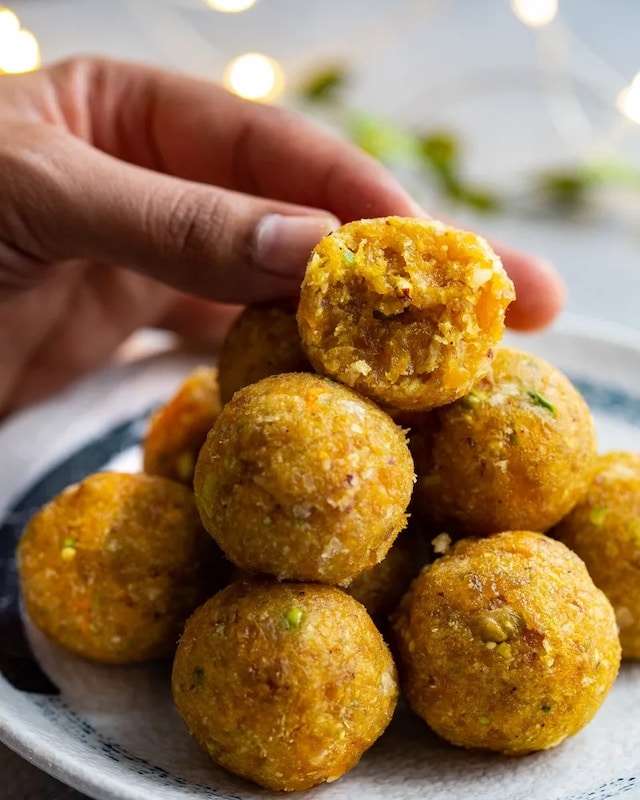 Spicy balls of apricots with pistachios and ginger, one of them is bitten and a woman's hand reaches for it.