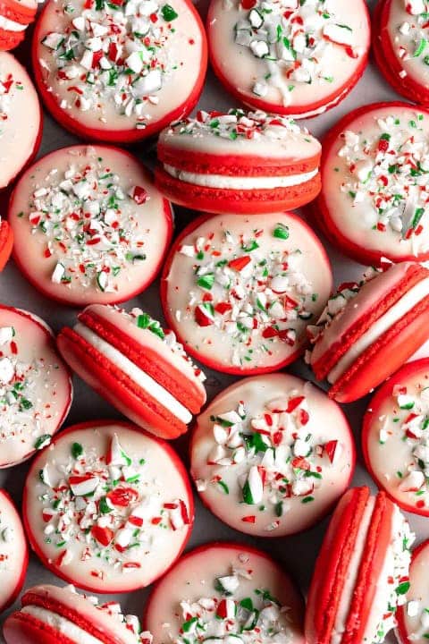 Red macarons filled with mint flavored buttercream and decorated with white chocolate frosting and sprinkles.