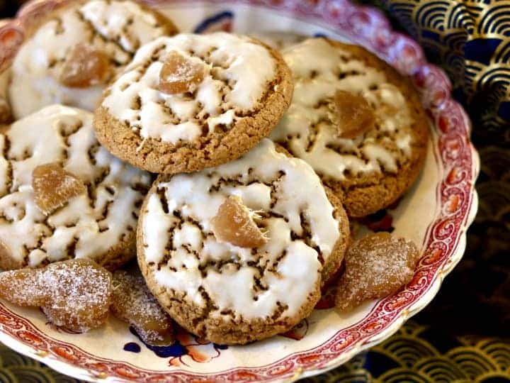 Rye cookies with icing and a piece of candied ginger on a plate.