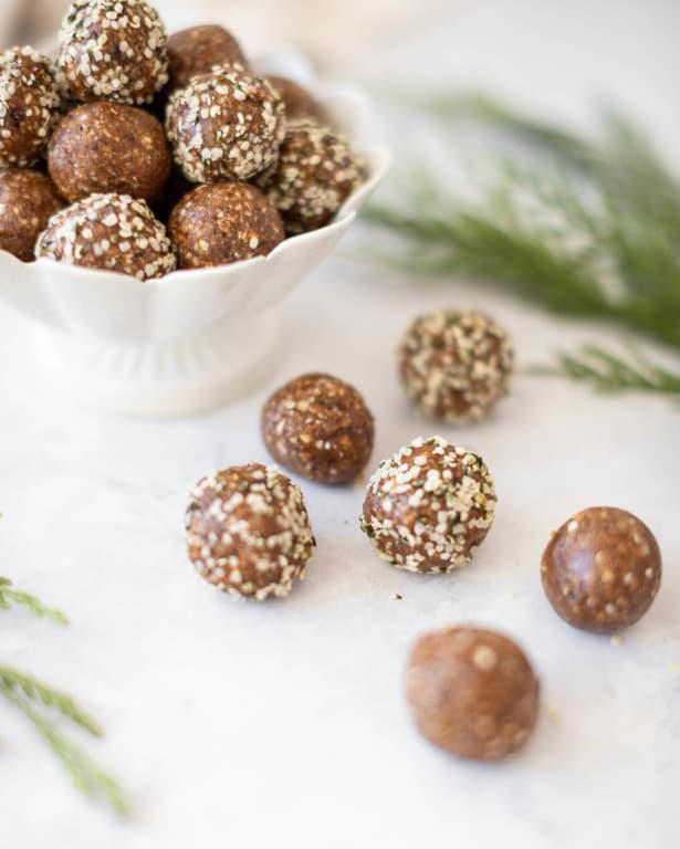 Balls of almonds, oatmeal, hemp seeds, nut butter, dates and gingerbread spice in a bowl. Other balls are placed next to the bowl.