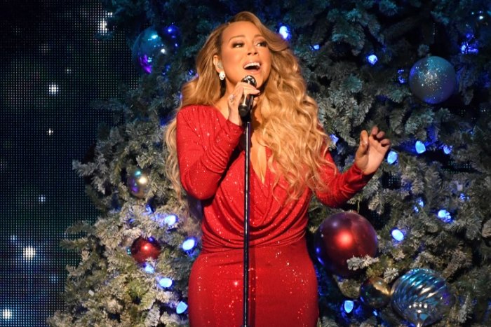 Mariach Carey sings in front of the Christmas tree.