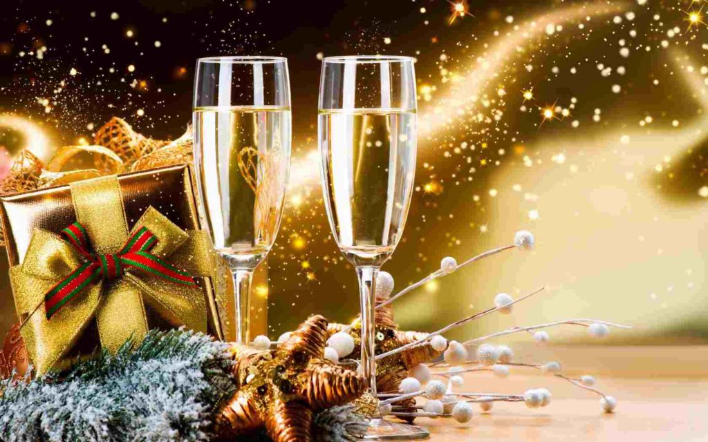 Golden background with gift with red and green bow and two full champagne glasses.