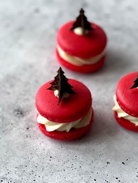 Red macaroons filled with whipped ginger-vanilla ganache and pear jelly and decorated with chocolate.