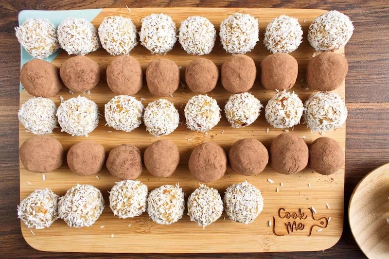 Apricot balls wrapped in coconut and cocoa on a wooden cutting board.