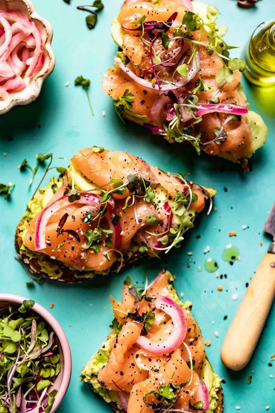 Avocado on a sandwich with salmon and onion.