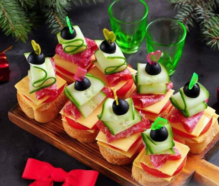 Canapés from a roll with fresh vegetables - tomato, cucumber and olive with a toothpick in the shape of decorative colorful hearts