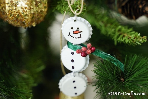 A Christmas snowman made of white corks, hanging on a branch of a Christmas tree.