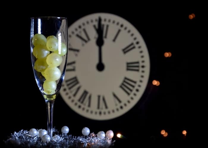 A glass with balls of grape wine and a clock striking midnight.