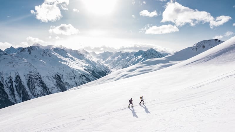 The couple walks to the top on a snowy plain.