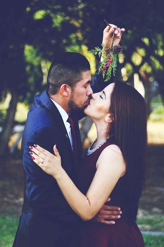 Young couple kissing under a mistletoe sprig.