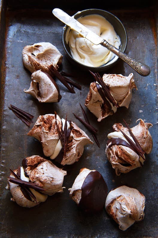 Chocolate meringues with cinnamon glued with apple snow and decorated with chocolate twigs. Next to the meringues is a bowl of apple snow with a knife.