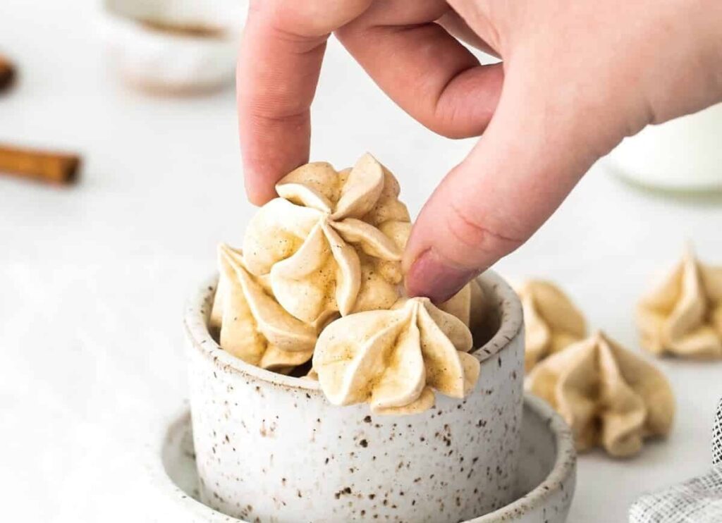 Cinnamon meringues in a bowl, and a hand scooping them up.